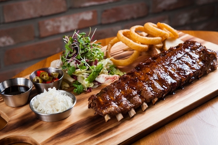 Barbecue rib with sprouts and onions rings, on wooden plate