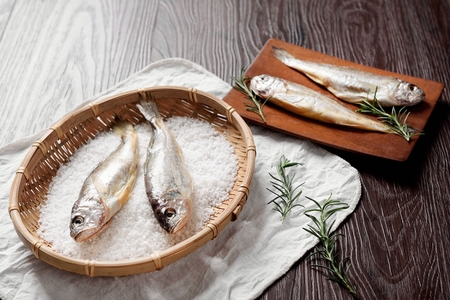 salted dry fish on wooden basket and also on wooden cutting boardの写真素材