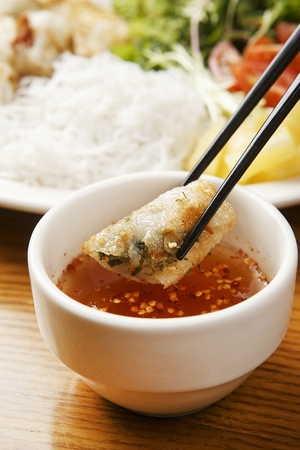 chopsticks dipping cha gio in sauceの写真素材