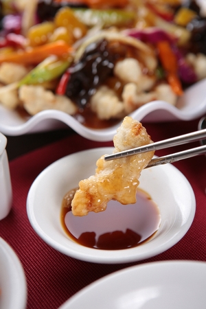 chopsticks grabbing sweet and sour pork over a small plate containing soy sauceの写真素材