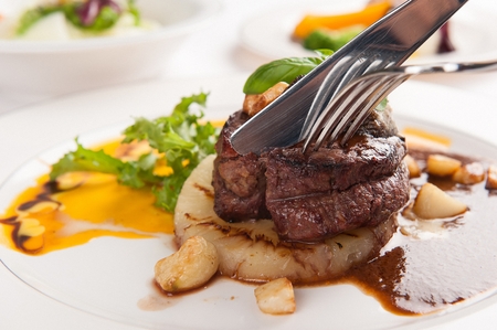 fork and knife cutting beef steak and pineapples on plate full of sauceの写真素材