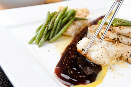 chopsticks dipping grilled toothfish in sauce
