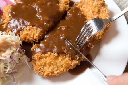 knife cutting fried pork cutlet with sauce on white plateの写真素材