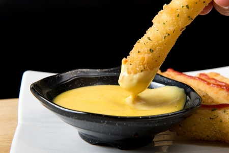hand dipping cheese stick into sauce with sprinkled parsleyの写真素材