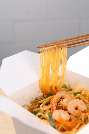 chopsticks grabbing phat tai with ingredients such as carrots, bean sprouts and shrimpの写真素材