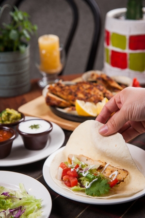 hand grabbing taco with tomatoes, vegetables and chickenの写真素材
