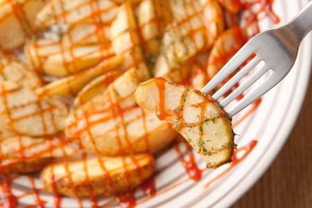 fork grabbing wedge potato with sauce, on plateの写真素材