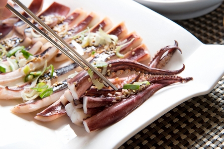 chopsticks grabbing parboiled squid on white plateの写真素材