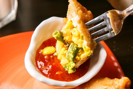 fork dipping half a samosa into sauceの写真素材