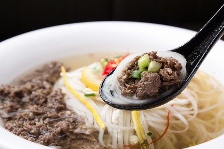 spoon scooping up rice noodles soup with meat