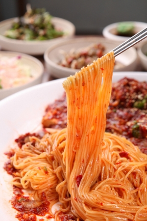 chopsticks grabbing noodles mixed with spicy braised pollacks with minced chiliの写真素材