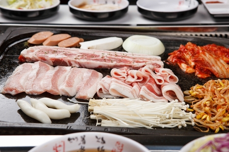 pork, onion and kimchi being barbecued on panの写真素材