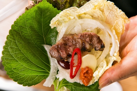 hand wrapping grilled pork with vegetables in lettuceの写真素材