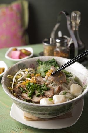 chopsticks grabbing rice noodles soup with meat and meatballs