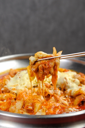 chopsticks grabbing spicy stir-fried chicken and various vegetables and cheeseの写真素材