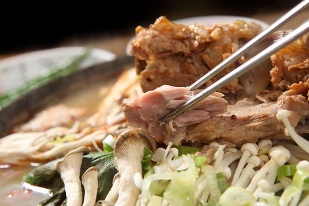 chopsticks grabbing meat from pork back-bone stew with various vegetablesの写真素材