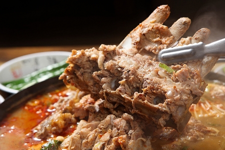 tongs grabbing meat from pork back-bone stew with various vegetablesの写真素材