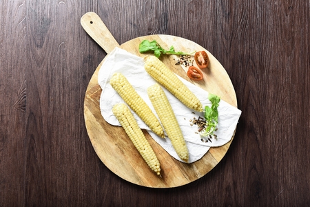 Yellow corn on wooden plate with handles and cherry tomatoesの写真素材