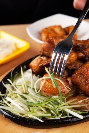 Seasoned spicy chicken with seasoned green onions on iron plateの写真素材