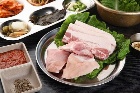 Raw pork belly with lettuce on top of steel plateの写真素材