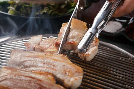 Grilled pork belly being cut with scissors and pincersの写真素材