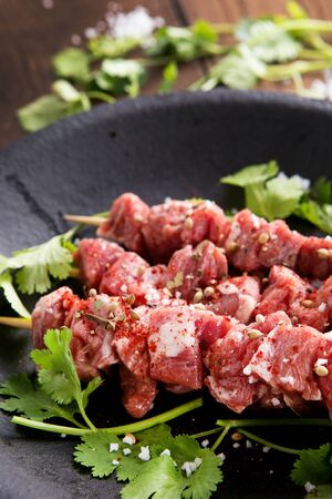 Seasoned uncooked skewered lamb with vegetables on black metal plateの写真素材