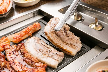 Pork  belly being grilled on grill, grabbed with pincersの写真素材