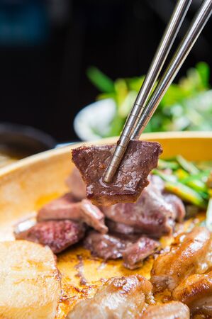 Chopsticks grabbing grilled heart cooked on grillの写真素材