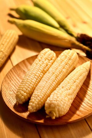 Open, cut corn on wooden plate and not cut, not open corn on plateの写真素材
