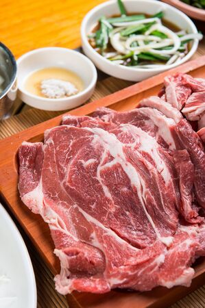 raw sirloin, seasoned vegetables and sauce on wooden plateの写真素材