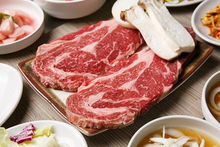 raw sirloin, mushrooms, side dishes on rectangular plateの写真素材