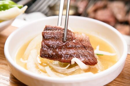 slice of meat and seasoned onions grabbed with chopsticksの写真素材