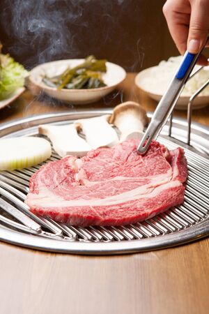 pincers grabbing raw sirloin on grill, with vegetablesの写真素材