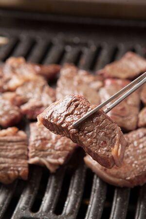 chopsticks grabbing a slice of meat on grillの写真素材