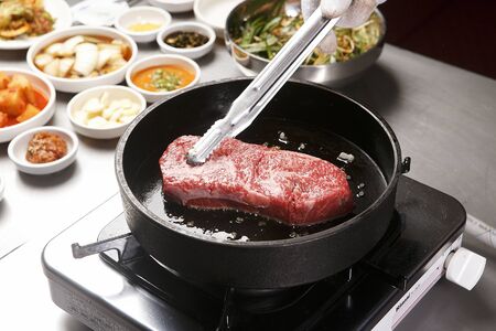 sirloin being cooked on grill, with side dishesの写真素材