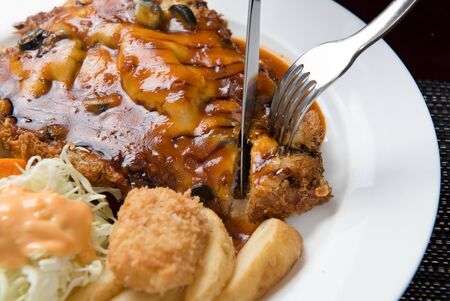 cutting Donkatsu with olive and cheese using fork and knifeの写真素材