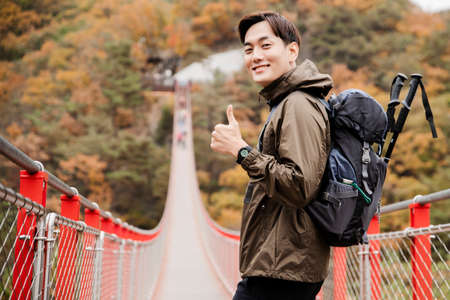 Asian handsome man with mask trekking, climbing autumn mountain