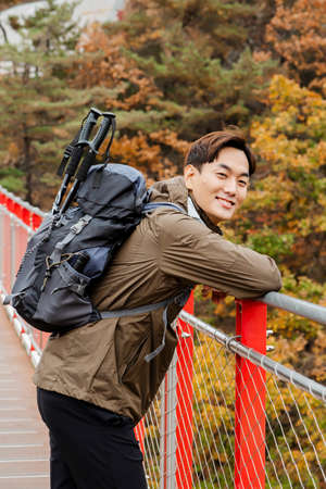 Asian handsome man with mask trekking, climbing autumn mountain