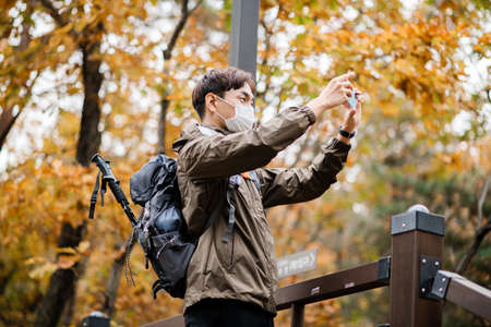 Asian handsome man with mask trekking, climbing autumn mountainの写真素材