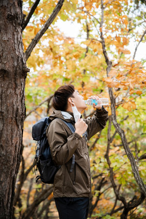 Asian handsome man with mask trekking, climbing autumn mountain
