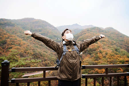 Asian handsome man with mask trekking, climbing autumn mountain