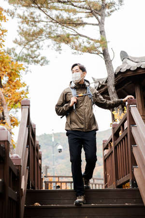 Asian handsome man with mask trekking, climbing autumn mountainの写真素材