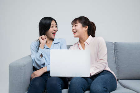 two Asian sisters, women on sofa using laptopの写真素材
