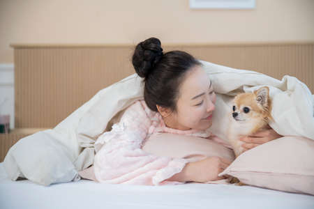 Asian woman in pajamas under blanket hugging puppy dog