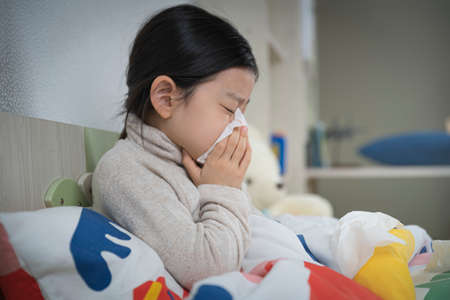 Asian little girl blowing nose on the bedの写真素材