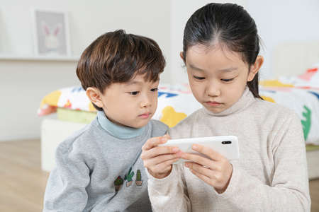 Asian girl and boy, sister and brother playing with smartphoneの写真素材