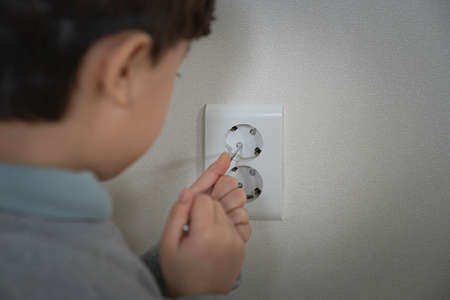 Asian boy inserting finger into an electrical outlet