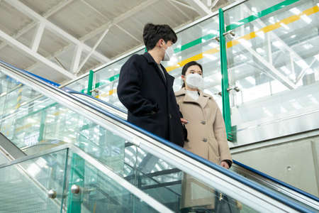 Asian couple on escalator with face masksの写真素材