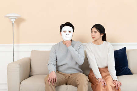 Asian husband holding a mask on his face and wife sitting next to him
