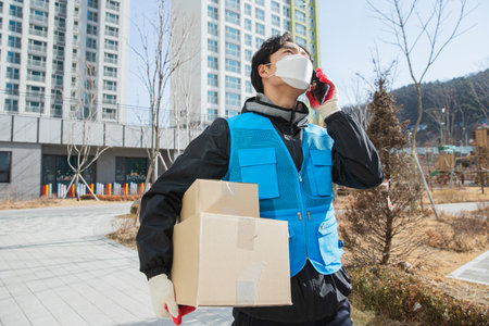 Asian delivery man with mask on phone with customerの写真素材